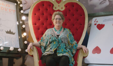 lady sits on throne nest to giant playing card